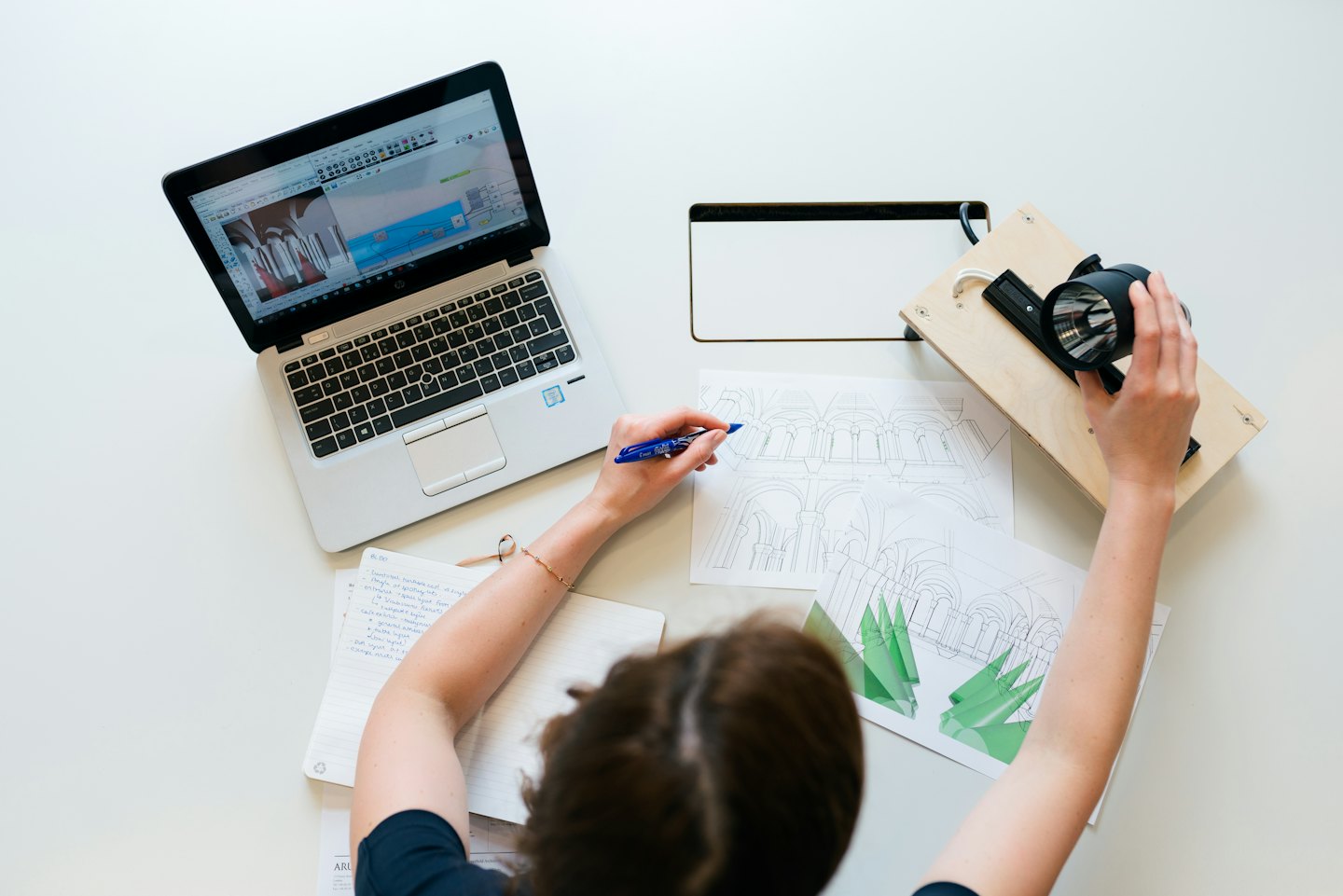 Un designer esquisse des plans de bâtiment à côté d'un ordinateur portable et d'un carnet.