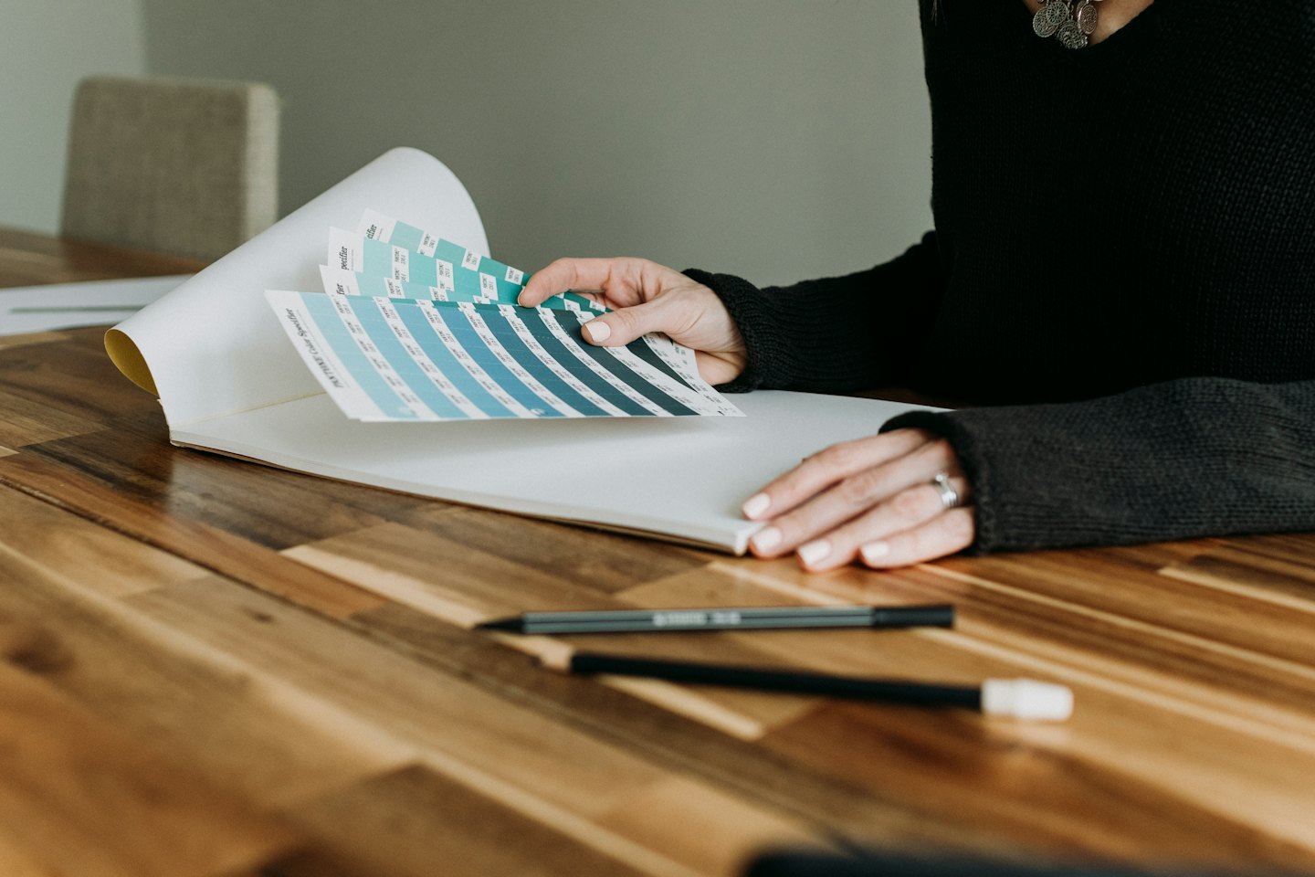 Mains créatives tenant un nuancier Pantone ouvert sur une table en bois.